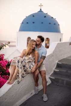 a man and woman sitting on the steps in front of a blue dome with pink flowers