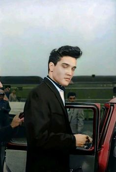 a man in a tuxedo getting out of a red car with his hand on the door handle