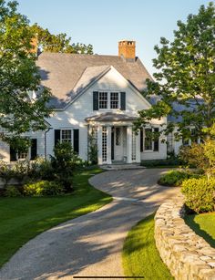 a white house with black shutters on the front and side windows, surrounded by green grass