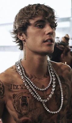 a young man with tattoos and jewelry on his chest is looking off to the side