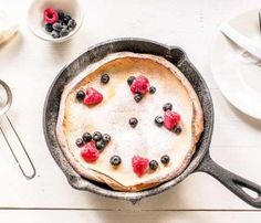 a pancake with berries and blueberries in it sitting on a table next to silverware