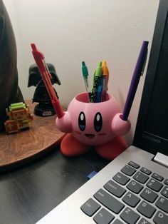 a desk with a laptop, pen holder and various office supplies on top of it