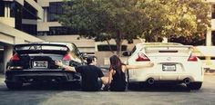 two people are sitting on the ground next to parked cars in front of a building