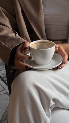 a person holding a coffee cup and saucer on their lap, while sitting in a chair