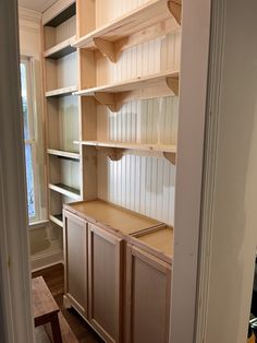 an empty room with wooden shelves and drawers on the wall, in front of a window