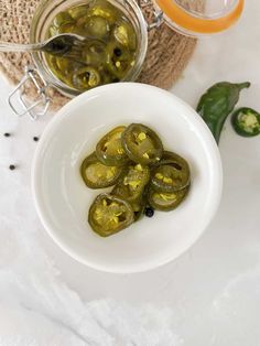 green peppers in a white bowl next to a jar of pickles