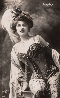 an old black and white photo of a woman in a dress with feathers on her head