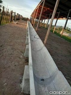 an empty dirt road next to a wooden fence and building with metal posts on the sides