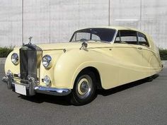 an old yellow car parked in front of a building