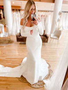 a woman in a white wedding dress taking a selfie with her cell phone while wearing a long sleeved gown