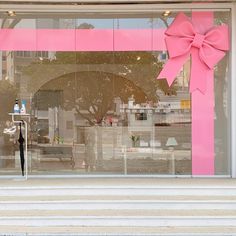 a large pink bow on the side of a store window with steps leading up to it