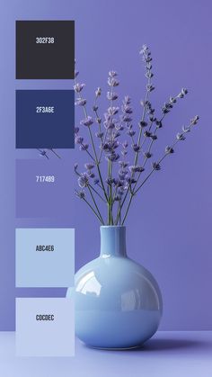 a blue vase filled with purple flowers on top of a white table next to a purple wall