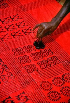 a person is working on a red and black table cloth with an intricate design in the center