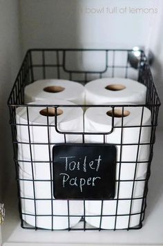 two rolls of toilet paper in a basket with a chalkboard on the side that says toilet paper