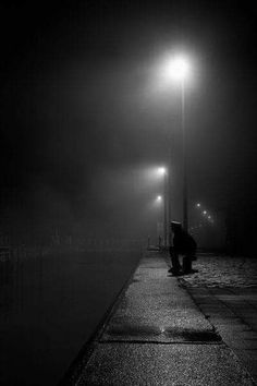 a person sitting on a bench at night with an umbrella over their head and street lights in the background