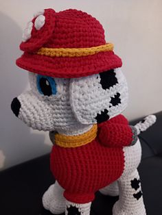 a crocheted stuffed dog wearing a red hat and scarf on top of a black table