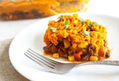 a close up of a plate of food with a fork on the side and a casserole in the background