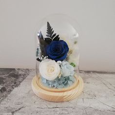 a blue rose and white flowers under a glass dome on a marble slabd surface