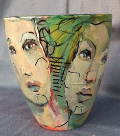 a close up of a vase on a green surface with two women's faces painted on it