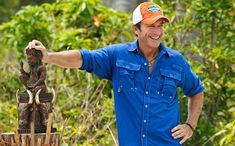 a man in blue shirt and orange hat standing next to an elephant statue with two elephants on it