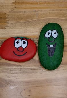 two rocks with faces painted on them sitting on top of a wooden table next to each other