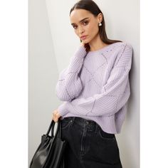 a woman leaning against a wall with her hand on her shoulder wearing a purple sweater