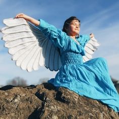 a woman sitting on top of a rock with an angel wings in her hand and arms outstretched