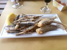 an image of fish on a plate with lemon wedges and wine glasses in the background