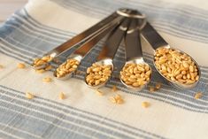 five measuring spoons filled with peanuts on top of a blue and white table cloth