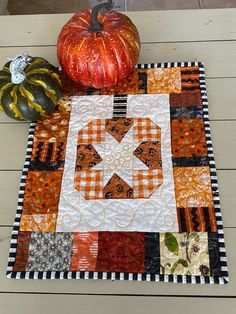 two pumpkins sitting on top of a table next to a quilted placemat