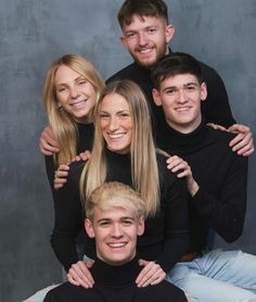 a group of young people posing for a photo in front of a gray wall with their arms around each other