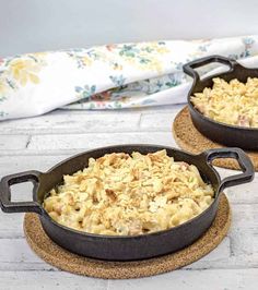 two cast iron skillets filled with macaroni and cheese on cork coasters