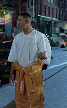 a man in white shirt and orange pants standing on sidewalk next to street with cars