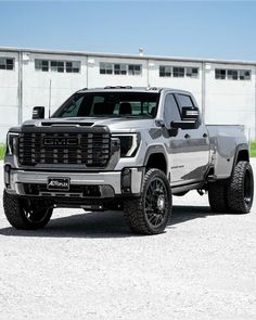 a silver truck is parked in front of a white building with black tires and rims