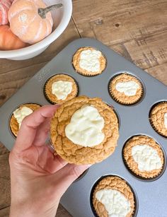 a person holding a cupcake in front of a muffin tin filled with frosting