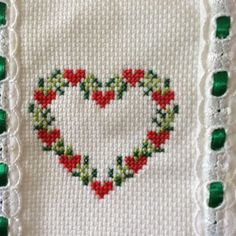 a cross stitched heart with red flowers and green beads on the border is displayed