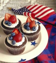 four cupcakes with strawberries and blueberries on top are sitting on a plate