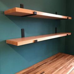 two wooden shelves are on the wall next to a wood floor and green painted walls