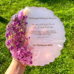 a person's hand holding a plate with flowers on it in front of green grass