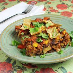 a green plate topped with lots of food on top of a floral table cloth next to a fork and knife