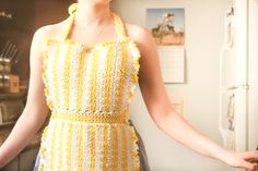 a woman wearing a crocheted yellow dress standing in front of a white refrigerator