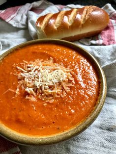 a bowl of tomato soup next to a loaf of bread