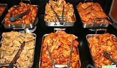 several trays of food with tongs and forks in them on a black table