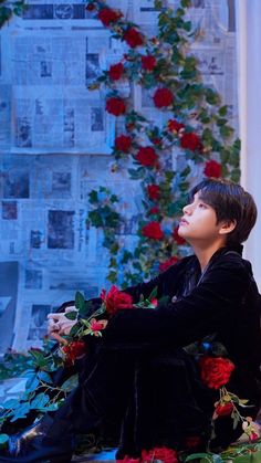 a young man sitting on the ground in front of a wall with roses and newspaper