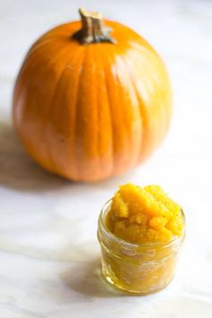 an orange pumpkin sitting next to a small jar filled with yellow food coloring and a smaller pumpkin in the background