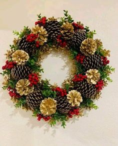 a christmas wreath with pine cones, holly berries and red berries on it is hung on the wall