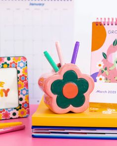 there is a flower shaped pen holder on top of the desk next to books and pencils