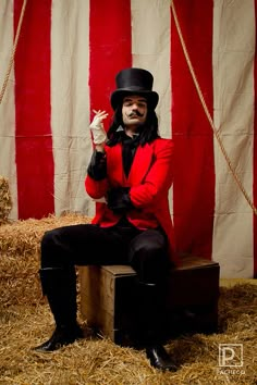 a man in a top hat and red jacket sitting on a box with his hands up