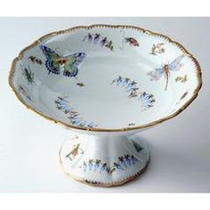 an ornate white bowl with gold trimmings and butterflies on the rim, sits in front of a white background