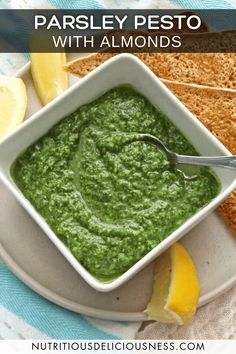 a bowl of pesto with lemon wedges on the side and toasted bread in the background